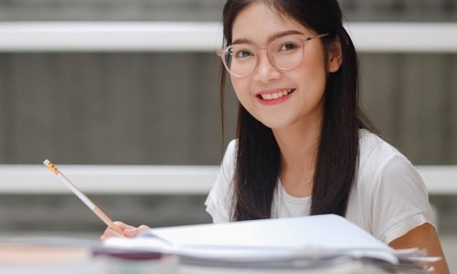 Asian student women reading books in library at university. Young undergraduate girl do homework, read textbook, study hard for knowledge and education on lecture desk at college campus.